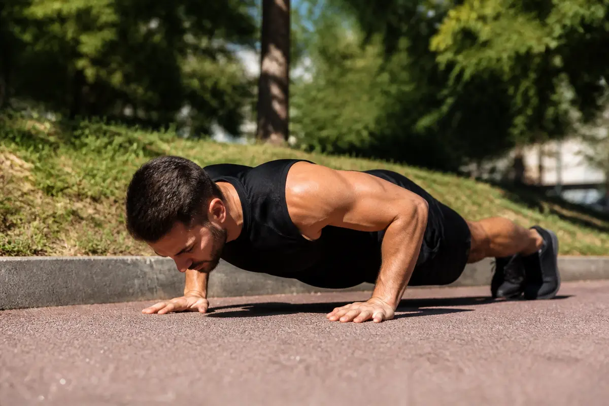 Homme réalisant des pompes pour renforcer pectoraux en plein air sur un trottoir.